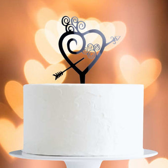 White cake with a decorative heart and arrow topper against a warm, blurred background.