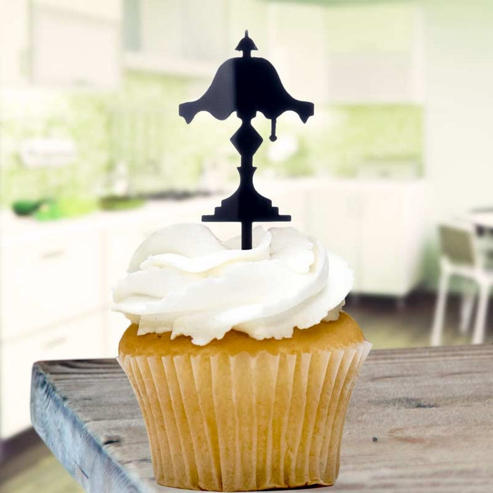 Cupcake with white frosting and a black decorative lampshade cupcake topper on a wooden surface.