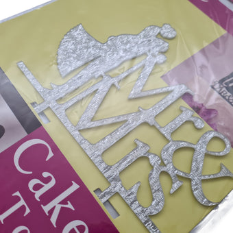 Silver cake topper with 'Mr' and 'Mrs' on a colourful background in packaging
