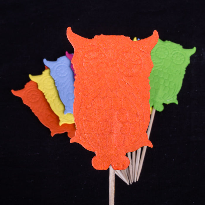 Colorful owl-shaped cupcake toppers on sticks against a black background