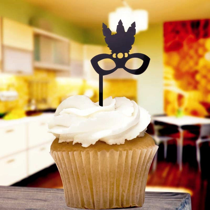Cupcake with white frosting and a black mask-shaped topper in a blurred indoor setting
