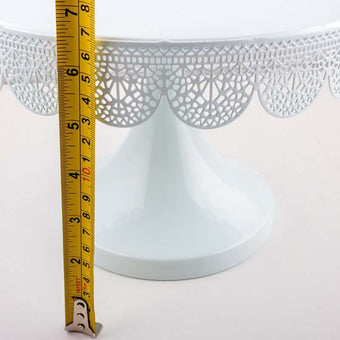White decorative cake stand with a measuring tape for scale on a white background