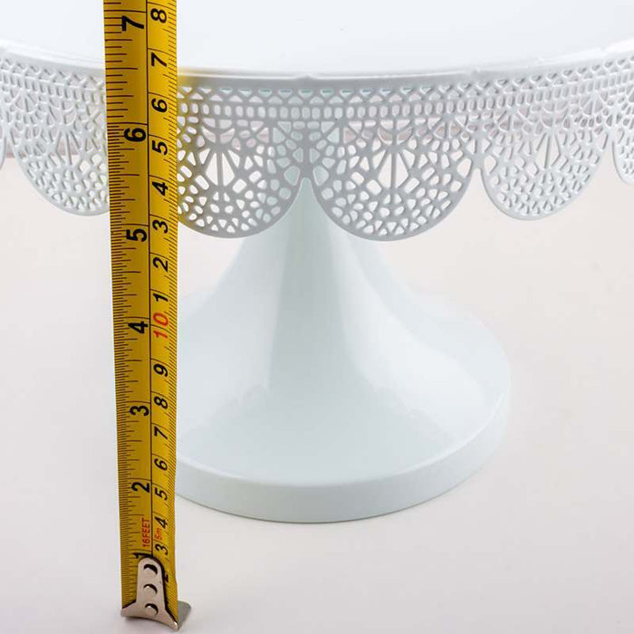 White decorative cake stand with a measuring tape for scale on a white background