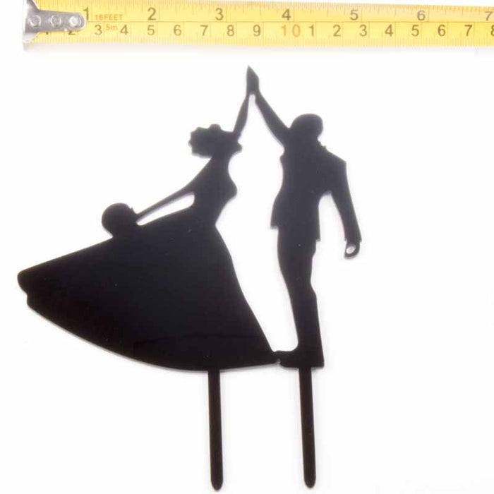 Silhouette of a bride and groom cake topper with a measuring tape at the top.