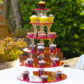 Red tiered cupcake stand with cupcakes on a table outdoors.