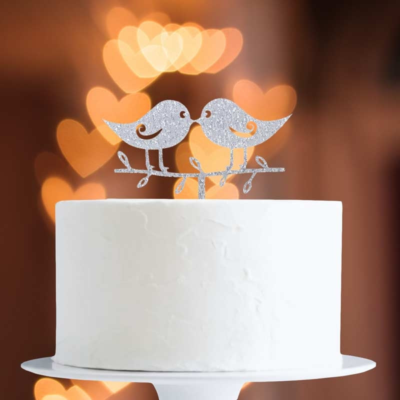 White cake with a decorative bird topper against a warm, blurred heart-shaped light background
