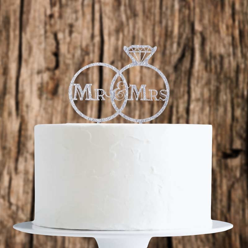 White cake with 'Mr & Mrs' ring cake topper against a wooden background