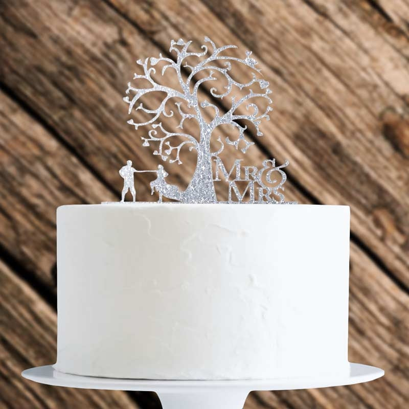 White cake with a silver 'Mr' and 'Mrs' tree topper against a wooden background